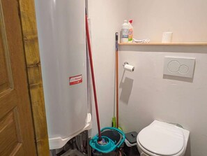 A bathroom with a white toilet, a red mop, a green bucket, and cleaning supplies on a shelf. - Cozy apartment with Mont-Blanc view - 6 guests (Hauteluce)