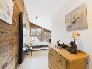 Ein Schlafzimmer mit schrägen Wänden, Holzwänden, einem Bett, einem Schminktisch und einem Gemälde.