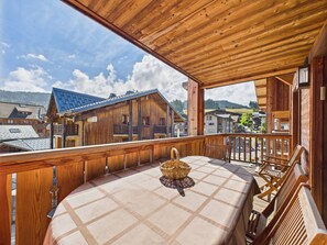 Ein Holzbalkon mit Tisch und Stühlen, der auf ein Dorf mit traditionellen Gebäuden blickt.