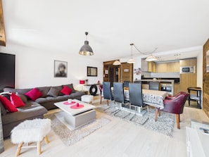 Ein modernes Wohnzimmer mit einer Couch, einem Esstisch und Stühlen. Es gibt eine Küchenzeile mit Holzschränken und einer Mikrowelle.