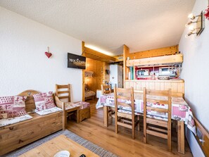 A cozy room with a wooden sofa, a dining table with chairs, a kitchen area, and a television mounted on the wall. - Apartment near slopes - 6 guests (Bourg-Saint-Maurice)