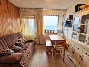A cozy room with a brown sofa, wooden dining table, and chairs. There's a cabinet with glass doors on the right. - South studio, pets welcome - 6 guests (Saint-Michel-de-Chaillol)