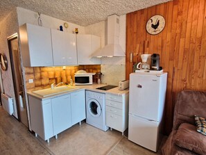 Een kleine keuken met witte apparaten, een wasmachine en een koffiezetapparaat.