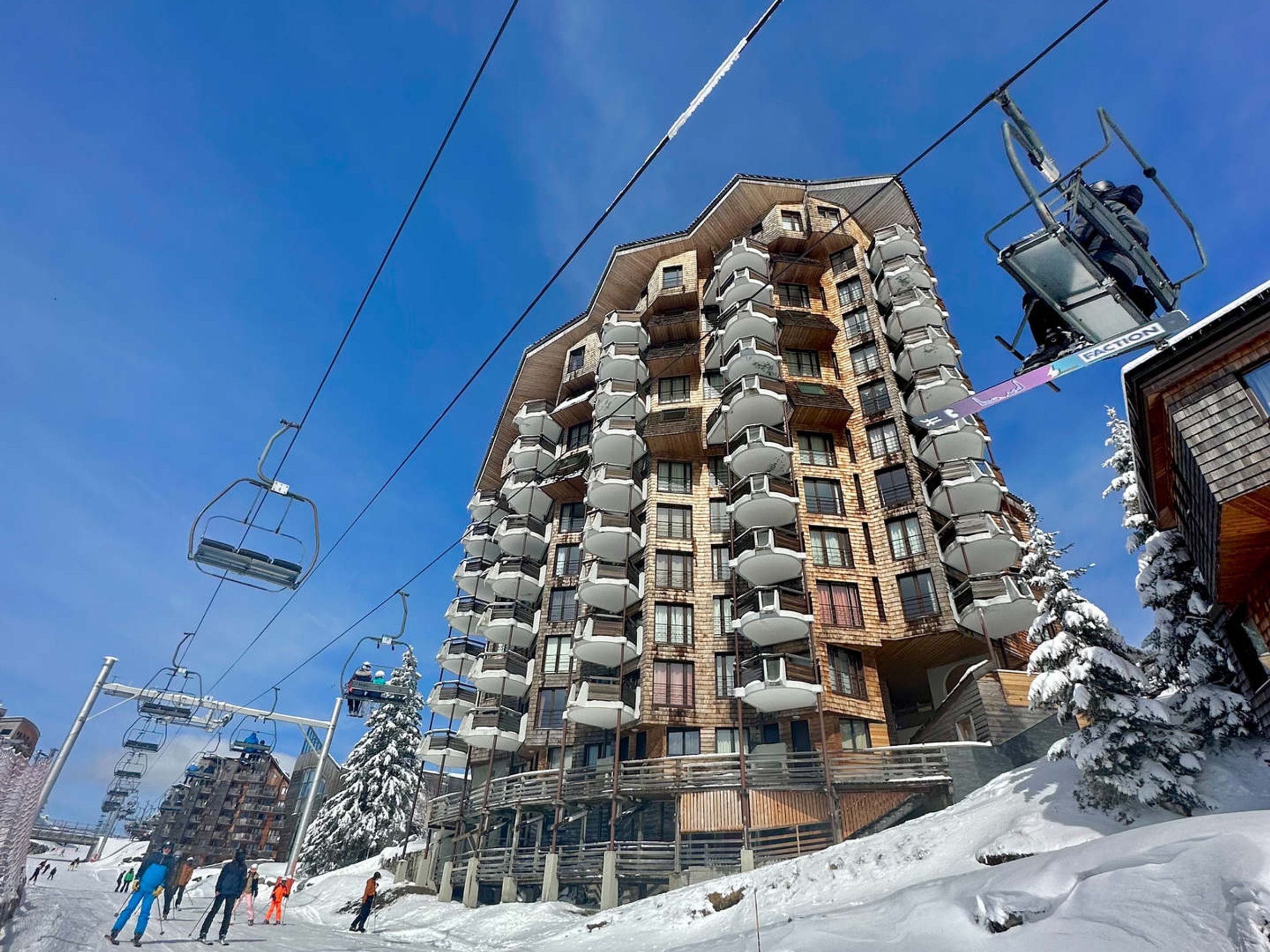 A multi-story hotel with balconies, ski lift cables, and snow-covered trees.