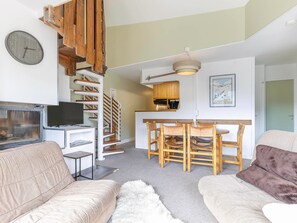A modern living room with a sofa, a television, a fireplace, and a staircase leading to a kitchen area. - Apartment with fireplace, mountain view - 8 guests (Avoriaz)