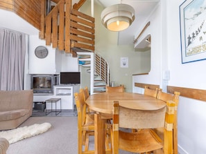 A dining area with a wooden table and chairs, a television, and a kitchen area with a stove. - Apartment with fireplace, mountain view - 8 guests (Avoriaz)