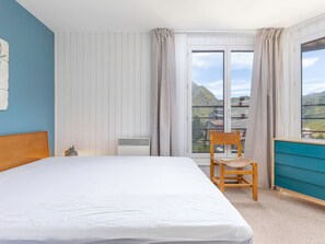 A hotel room with a bed, a chair, a dresser, and a view of mountains through the window. - Apartment with fireplace, mountain view - 8 guests (Avoriaz)