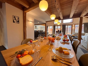 A dining area with a long wooden table set for a meal, featuring clear glassware, plates with fruits, and bread. - Large chalet - 16 guests (Vars)