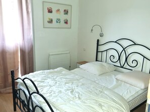 A single bed with a white mattress and a black metal frame in a room with a white wall and a radiator. - Apartment with parking and pets - 6 guests (Les Gets)
