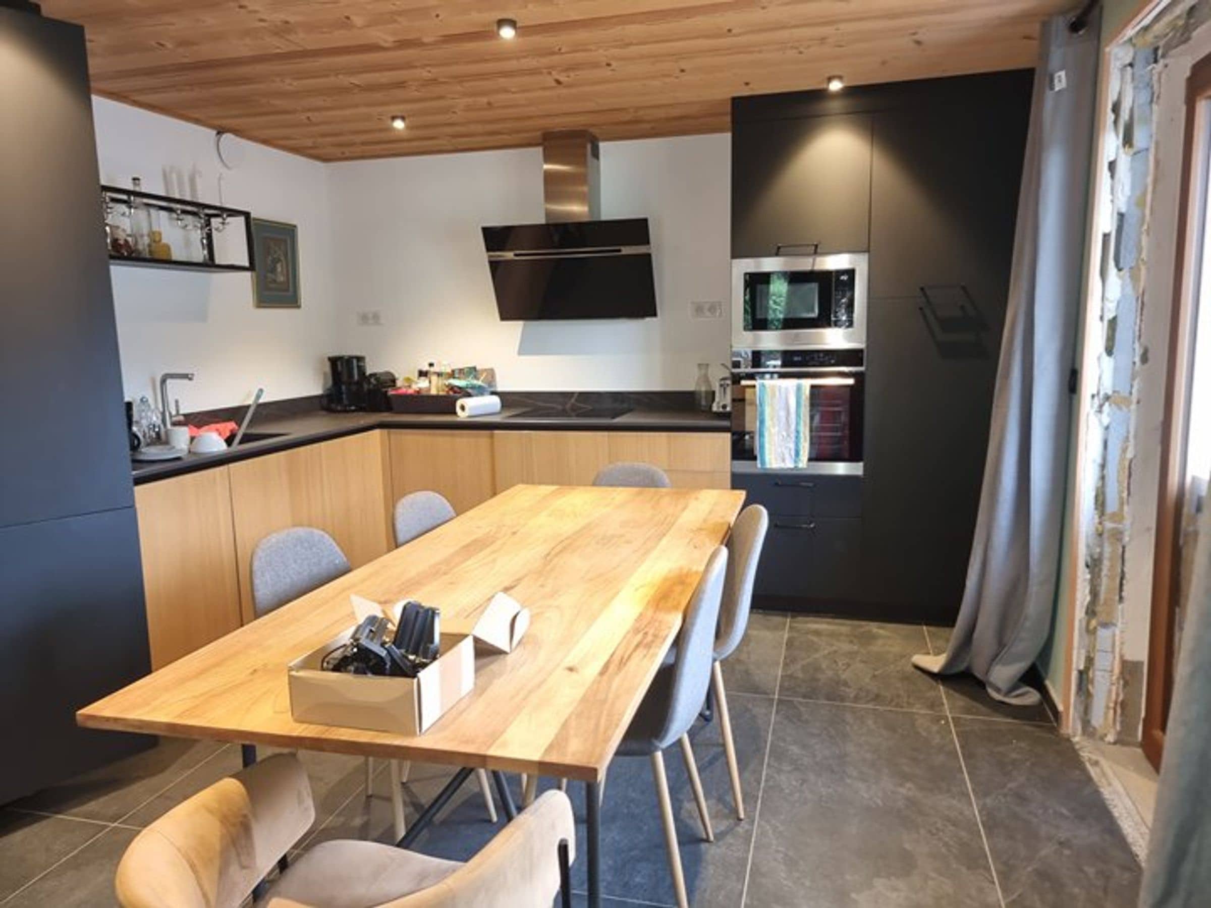 A modern kitchen with a wooden dining table, chairs, and built-in appliances.