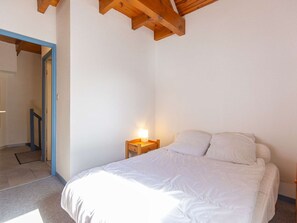 A bedroom with a bed, a nightstand, and a wooden ceiling beam. - Cozy duplex apartment with view - 6 guests (Esquièze-Sère)