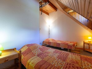 Ein Schlafzimmer mit zwei Betten, einem Nachttisch, einer Lampe und einer Holzbalkendecke.