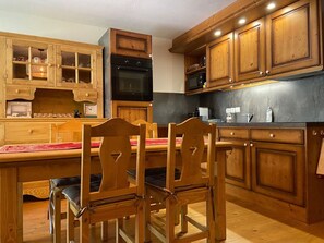 Cozinha com armários de madeira, mesa de jantar com cadeiras e forno embutido.