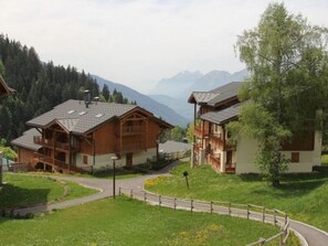 A wooden chalet with a balcony, surrounded by lush greenery and mountains in the background. - T3 Apartment with WIFI - 4/5 guests, south balcony (Crest-Voland)