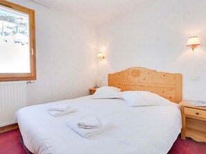 A hotel room with a wooden headboard, a bed with white linens, two bedside tables, and a window with a view of trees. - Spacious apartment, ski-in/ski-out - 6 guests (Les Menuires)