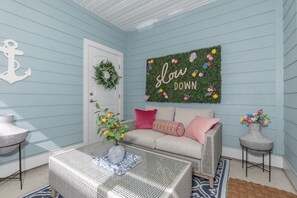 Quarto com parede azul clara, porta branca, sofá com almofadas rosa e listradas, mesa de centro com um vaso de flores e decoração de parede com a frase 'Love Down'.