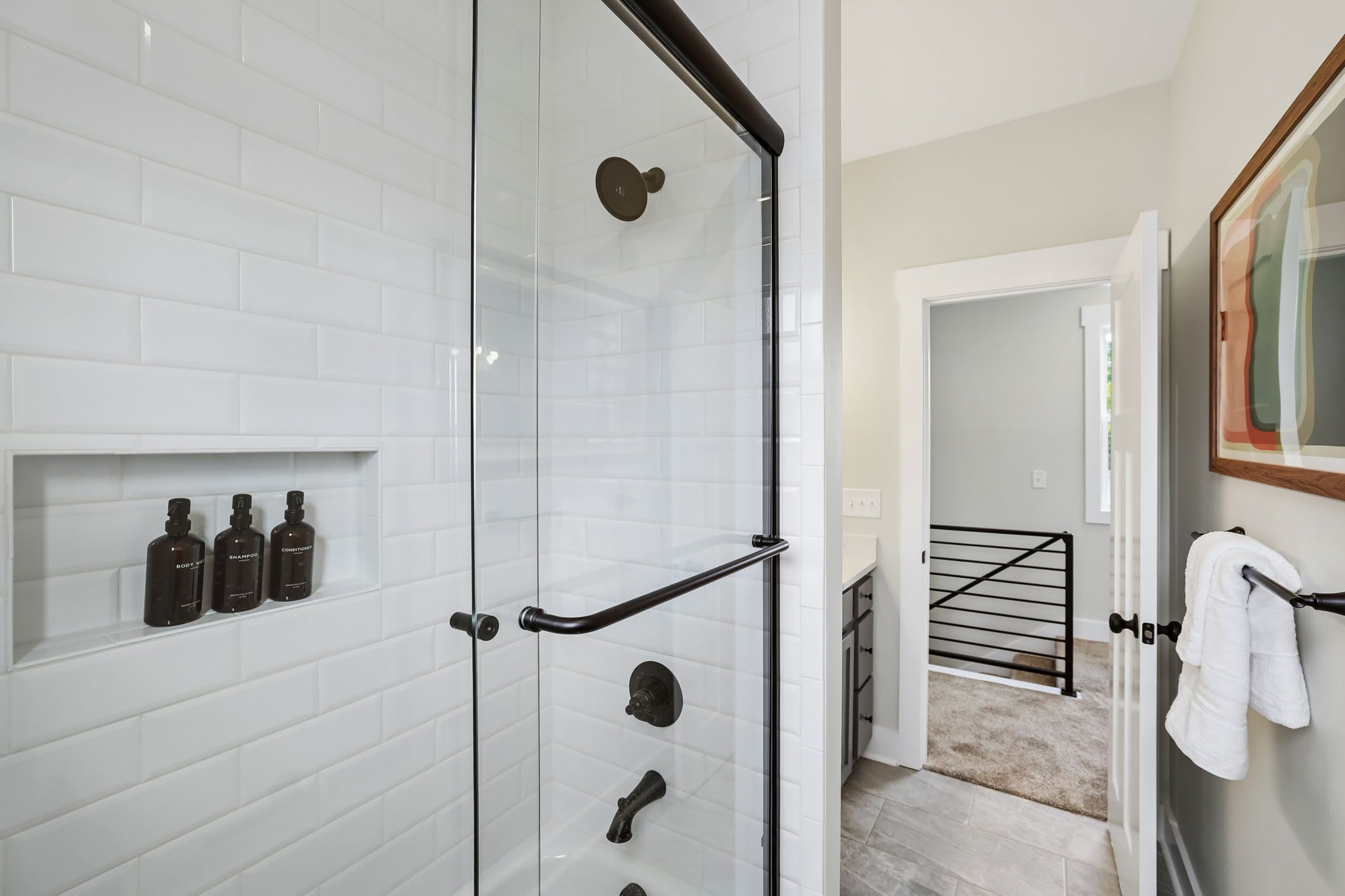 Une salle de bain moderne avec une douche à parois de verre, des carreaux de céramique blancs rectangulaires et un porte-serviettes avec une serviette blanche.