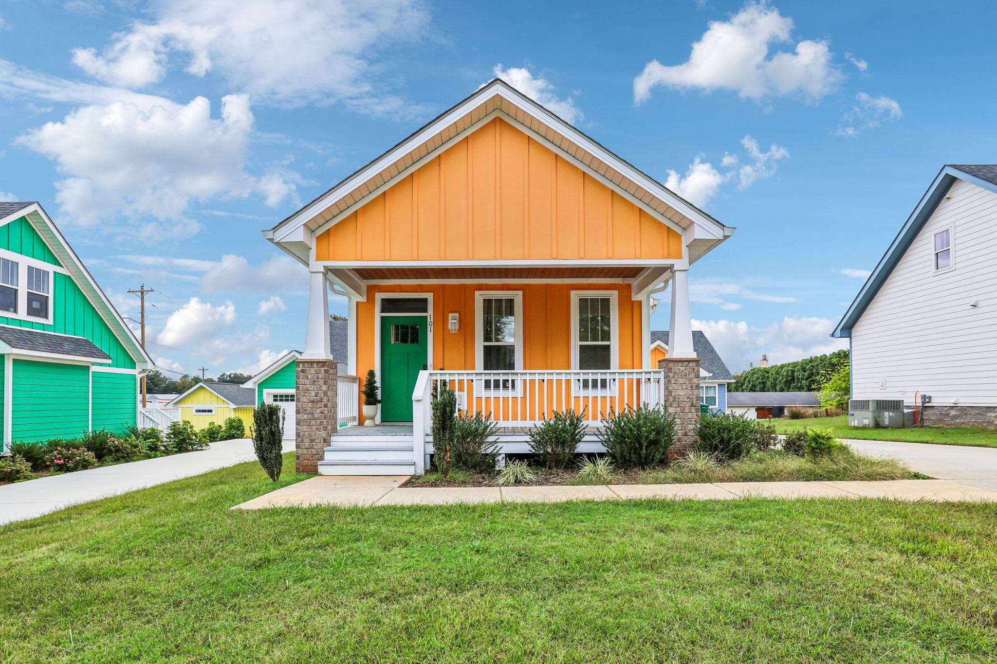 A single-story house with a front porch, a green door, and a white railing.