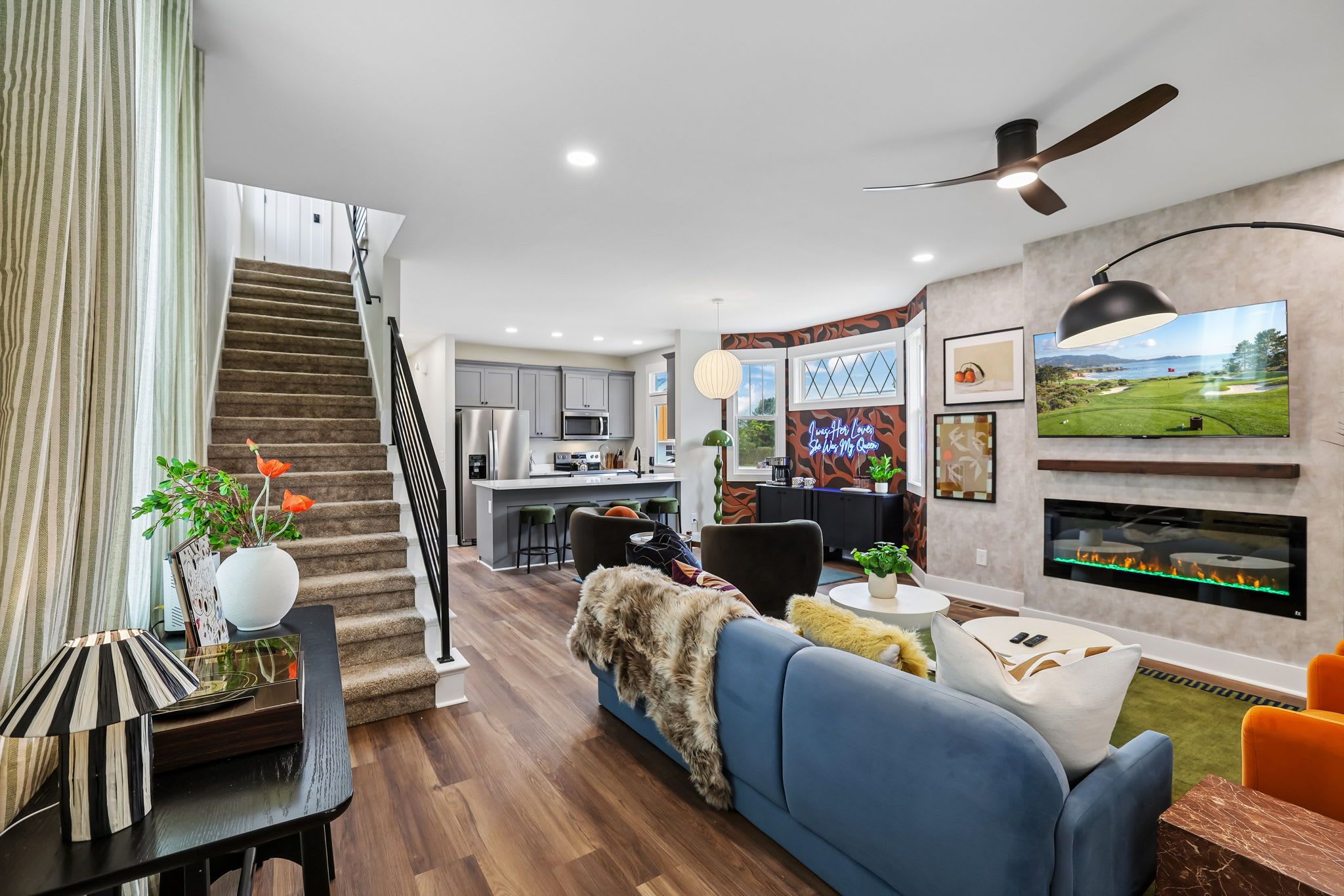 A modern living room with a blue sofa, a staircase, a kitchen, and a fireplace.