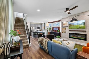 A modern living room with a blue sofa, a staircase, a kitchen, and a fireplace. - Iconic Winchester home near Tims Ford State Park! (Winchester)