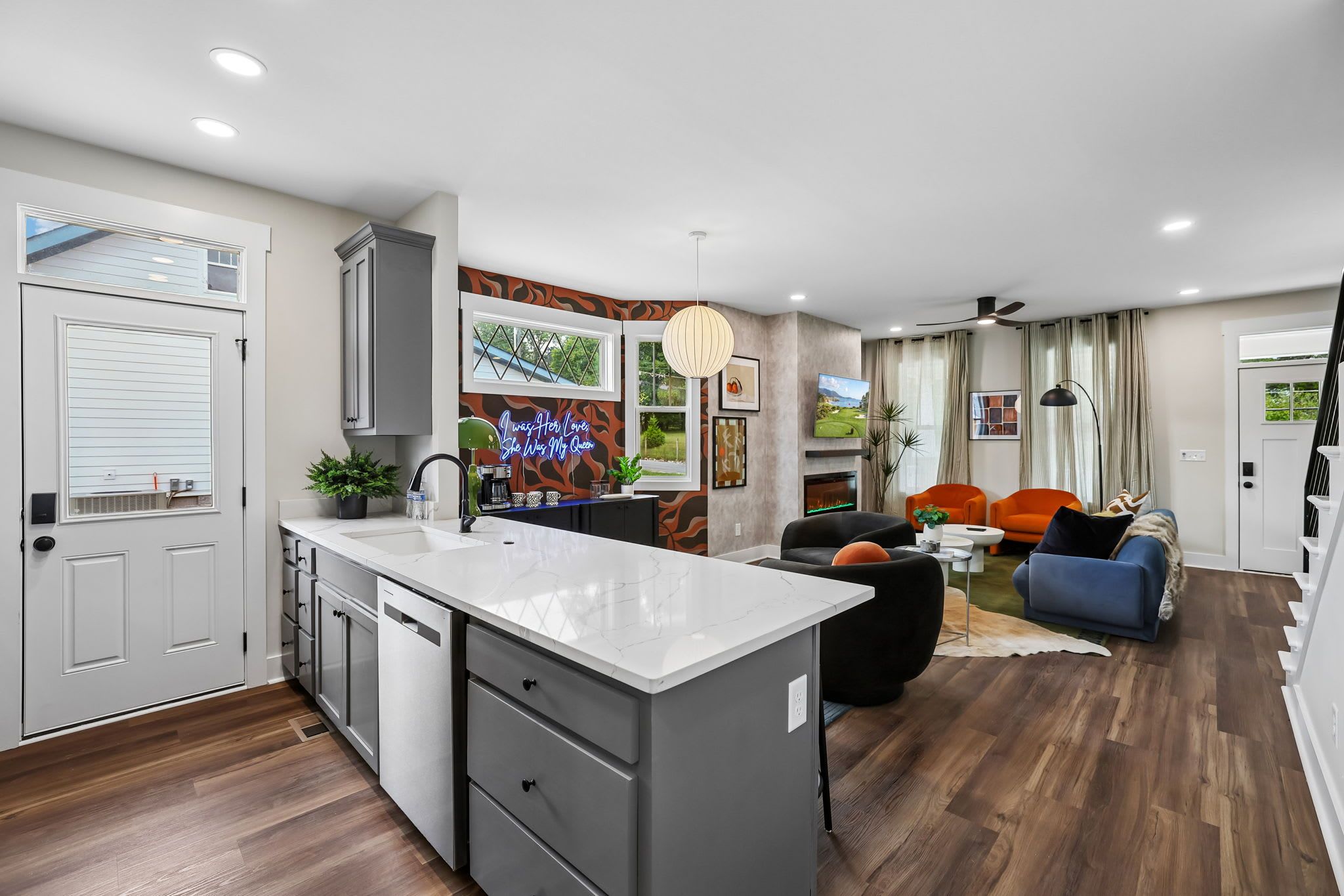 A modern kitchen with a central island, a dining area with a sofa and chairs, and a living room with a fireplace.