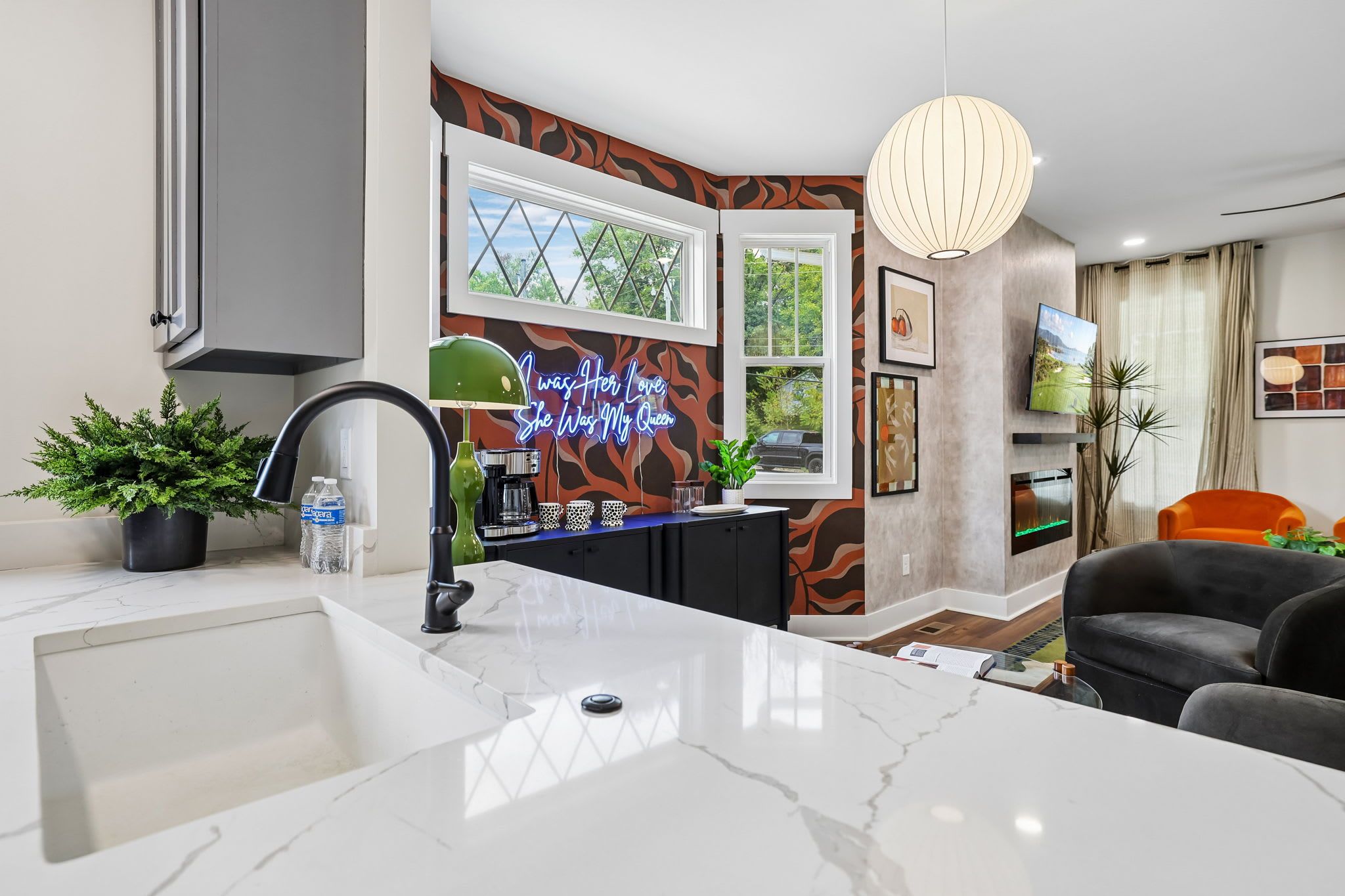 A modern kitchen with a marble countertop, a built-in oven, and a neon sign on the wall.