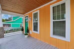 Une véranda en bois avec une balustrade, une porte verte et une vue sur la maison voisine.