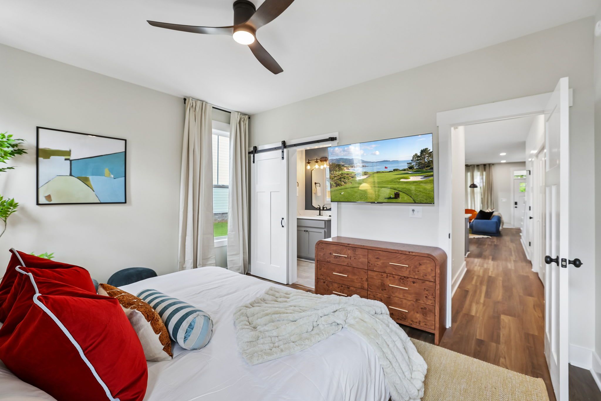A bedroom with a bed, a dresser, a TV, and a view of a golf course through an open door.