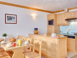 A wooden dining table with chairs, a small island with a microwave, and a tiled backsplash in the kitchen. - Spacious apartment ski-in/ski-out - 8 guests (Les Menuires)