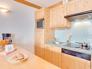 Una cocina con armarios de madera, un salpicadero de azulejos azules, un lavamanos de acero inoxidable y un lavavajillas.