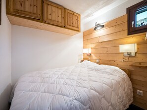 A bedroom with a wooden headboard, a white bedspread, and a wall-mounted light fixture. - Cozy apartment near slopes - 4 guests (Les Menuires)