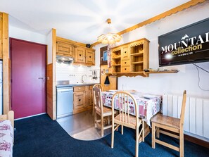 Une cuisine de taille réduite, avec des meubles en bois, une porte rouge et une table à manger accompagnée de chaises.