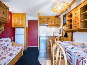Une cuisine compacte dotée de meubles en bois, d’un réfrigérateur, d’un évier et d’un coin repas avec une table dressée pour deux personnes.