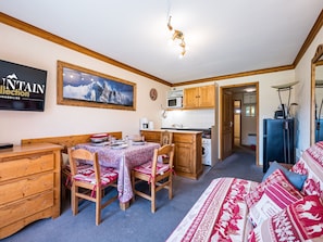 A compact room with a dining table, chairs, a sofa, a kitchen area with a microwave, and a washing machine. - Spacious apartment at the slopes - 5 guests (Les Menuires)