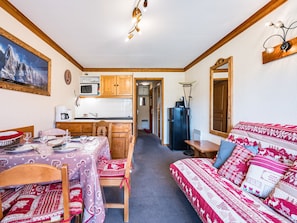 A compact living space with a kitchenette, a dining area, and a sofa with patterned cushions. - Spacious apartment at the slopes - 5 guests (Les Menuires)