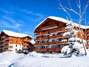 A multi-story wooden building with balconies, surrounded by snow. - Spacious apartment - 8 guests ski-in/ski-out (Les Menuires)