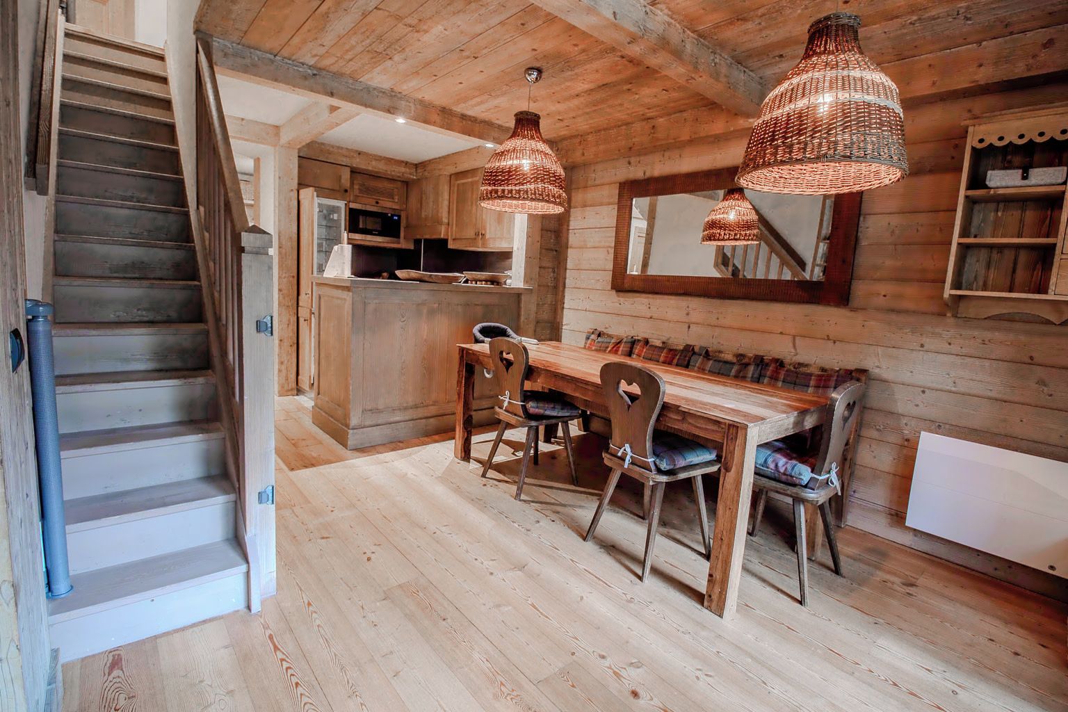 A wooden interior with a staircase, a dining area with a table and chairs, and hanging pendant lights.
