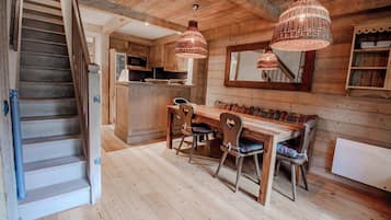 A wooden interior with a staircase, a dining area with a table and chairs, and hanging pendant lights.
