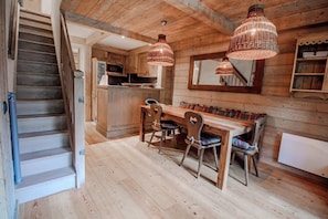 A wooden interior with a staircase, a dining area with a table and chairs, and hanging pendant lights. - Roche des Fours 210 (Val-d'Isère)