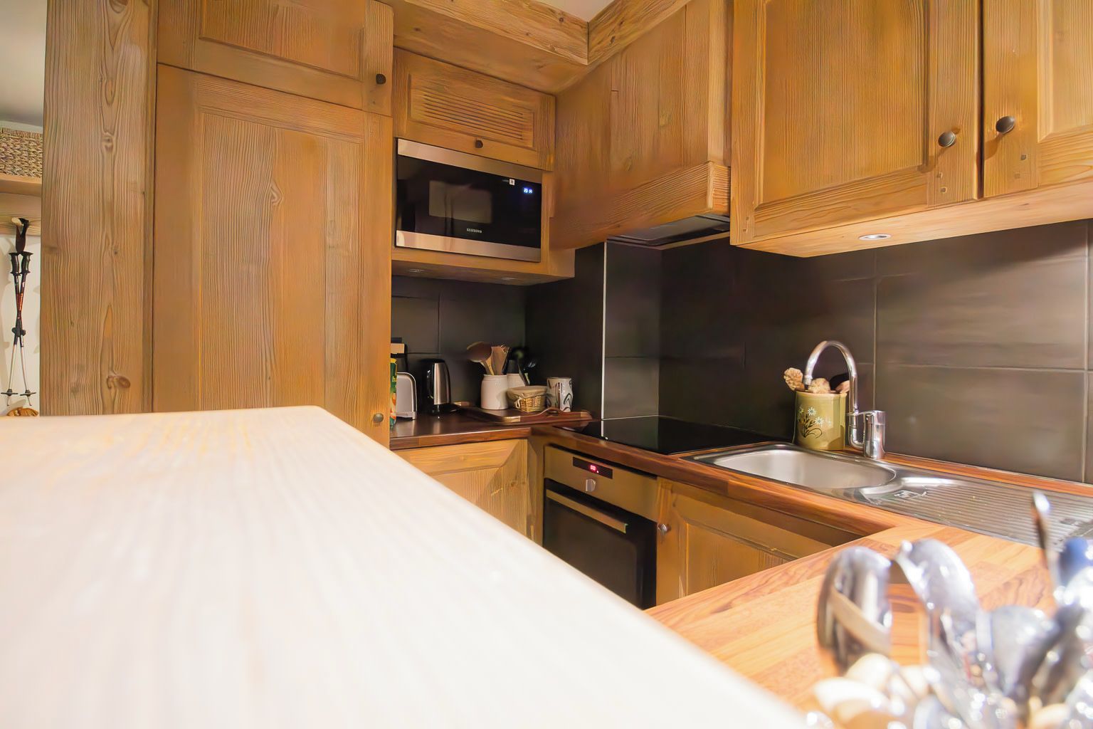 A kitchen with wooden cabinets, a microwave, a stainless steel sink, and a countertop with various kitchen items.