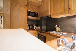 A kitchen with wooden cabinets, a microwave, a stainless steel sink, and a countertop with various kitchen items. - Roche des Fours 210 (Val-d'Isère)