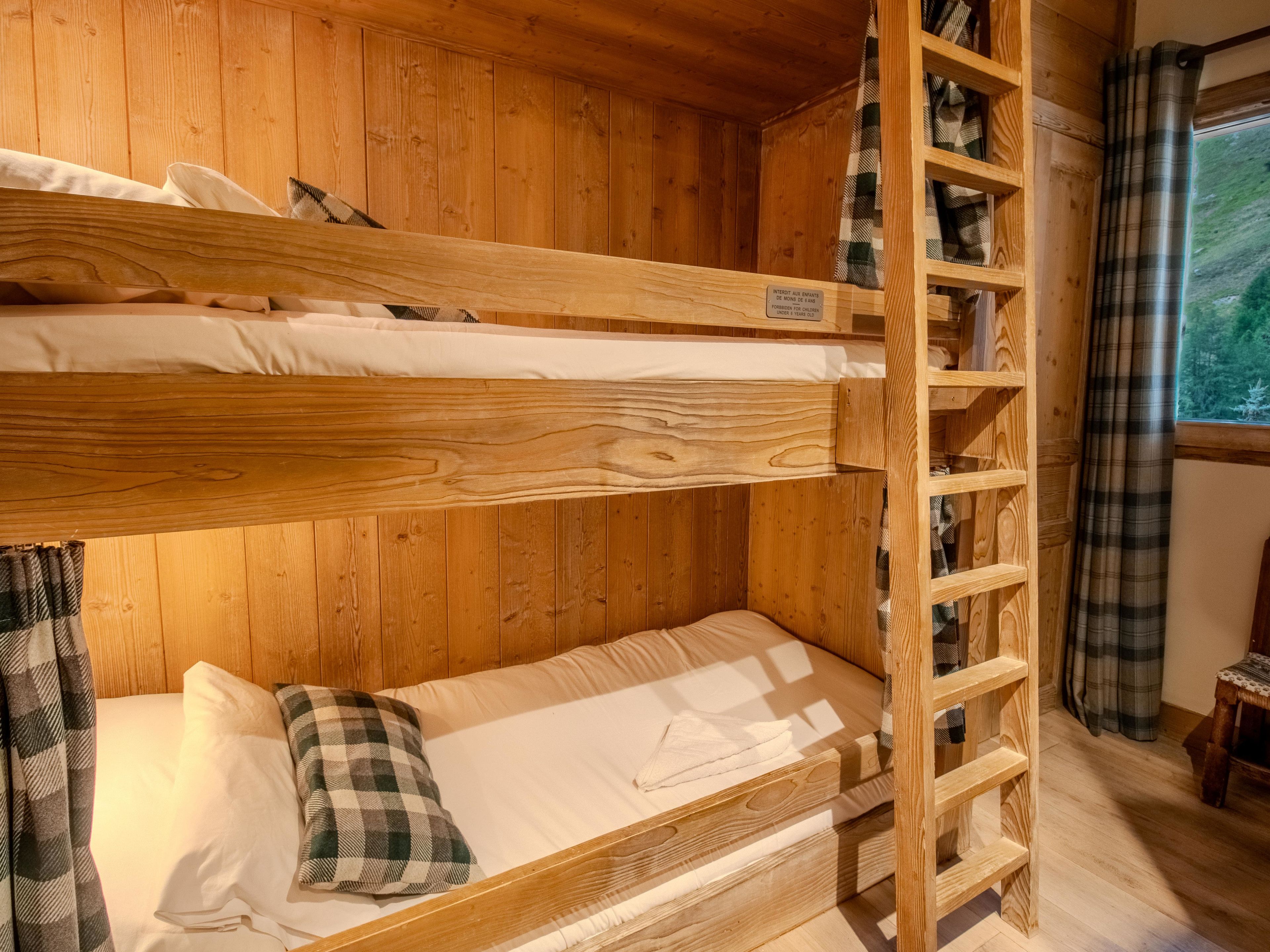 A bunk bed with a wooden ladder, a plaid pillow, and a shelf unit against a wooden wall.