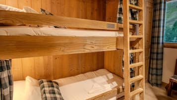 A bunk bed with a wooden ladder, a plaid pillow, and a shelf unit against a wooden wall.