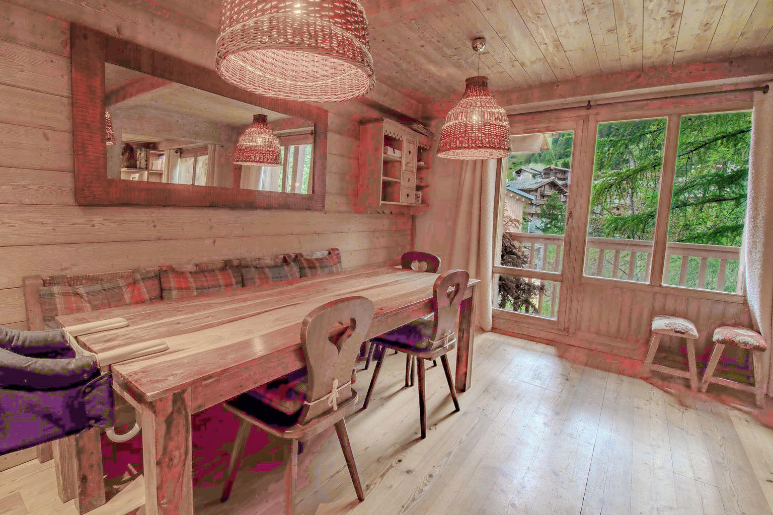 Un comedor rústico de madera con un banco, sillas y una mesa. Hay dos lámparas colgantes y un ventanal con vistas a la vegetación.
