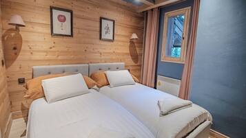 Una cama doble con dos almohadas y una colcha, paredes de paneles de madera, una ventana con cortinas y lámparas fijadas a la pared.