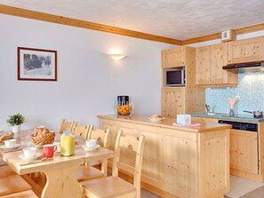 A wooden dining table with chairs, a small island with a microwave, and a tiled backsplash in the kitchen. - Spacious apartment, ski-in/ski-out - 8 guests (Les Menuires)