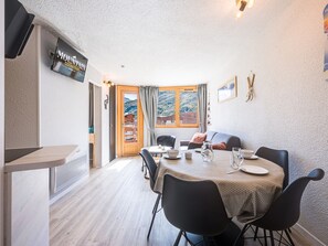 A dining area with a table set for four, a sofa, and a view of a mountainous landscape through a glass door. - Comfortable apartment with mountain view - 4 guests (Les Menuires)
