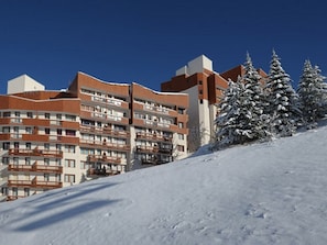 A multi-story hotel with balconies, snow-covered trees, and a clear blue sky. - Comfortable apartment with mountain view - 4 guests (Les Menuires)
