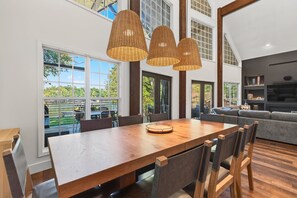 A dining area with a wooden table and chairs, large windows, and a view of the outdoors. - The Treehouse, Sleeps 12, Waterfront, Game Room, Firepit, Kayaks + MORE! (Milledgeville)