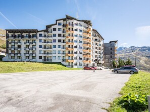 A multi-story hotel with balconies, a parking area, and a mountainous backdrop. - Pleasant apartment, near slopes - 4 guests (Les Menuires)